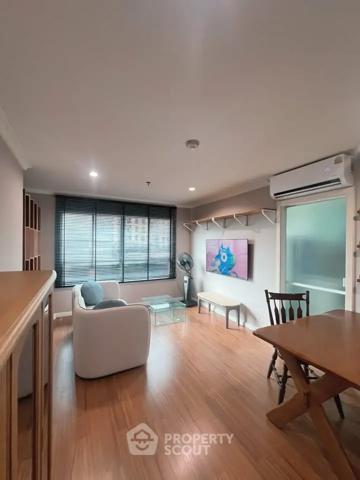 Modern living room with wooden flooring, stylish furniture, and large window offering natural light.