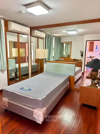 Spacious bedroom with mirrored wardrobe and wooden flooring in modern apartment.