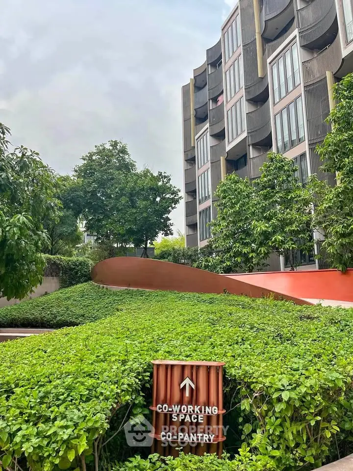 Modern building exterior with lush greenery and signage for co-working space and pantry.