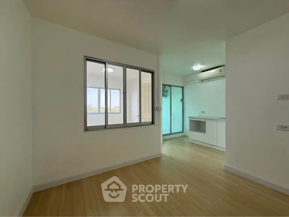 Spacious unfurnished room with wooden flooring and large window, perfect for customization.