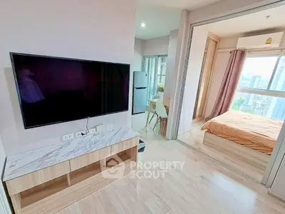 Modern apartment interior with open living room and bedroom, featuring sleek TV setup and city view.