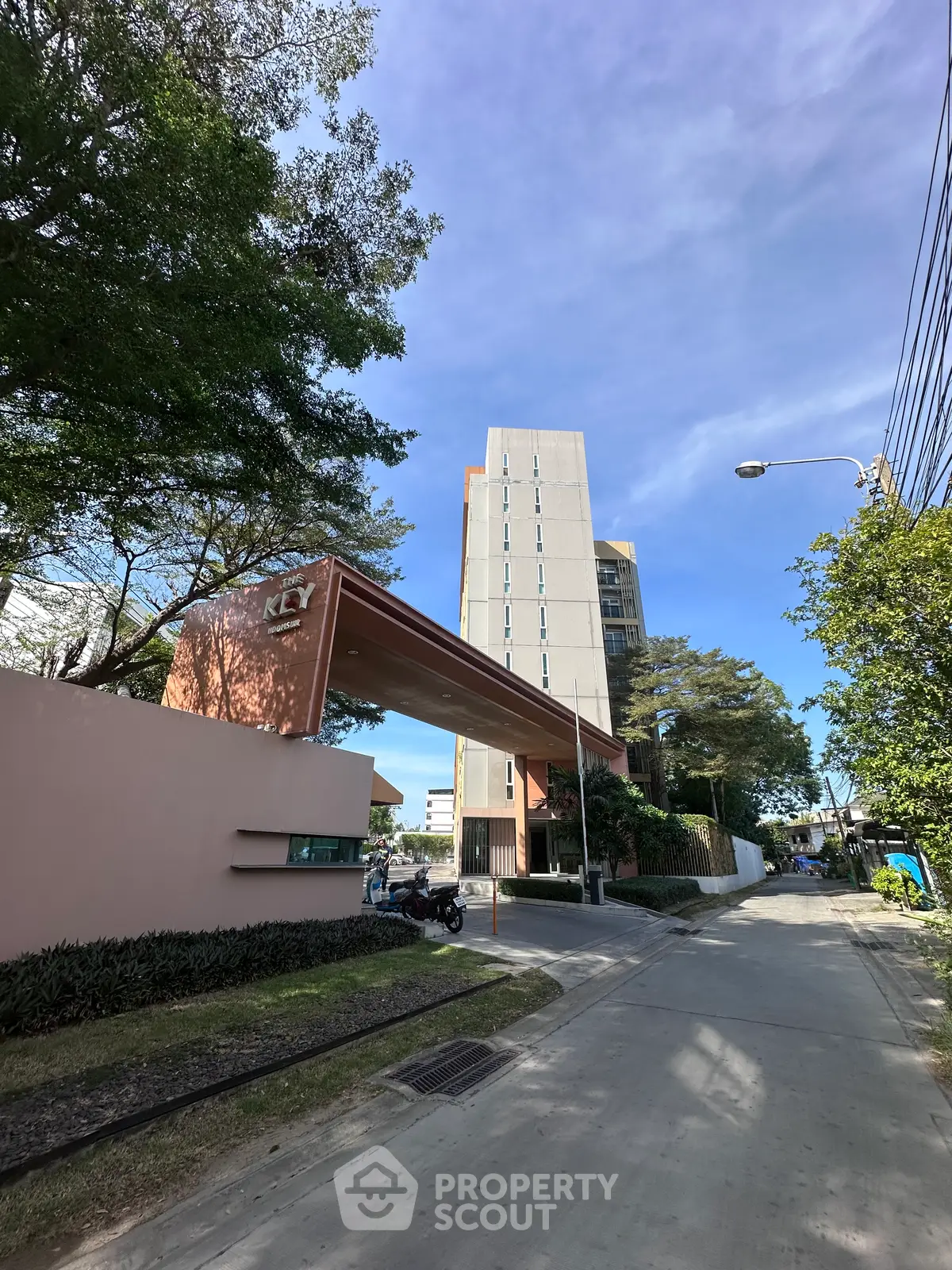 Modern high-rise building entrance with lush greenery and clear blue sky