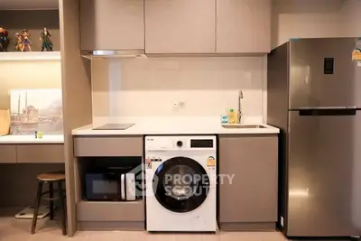 Modern kitchen with washing machine, microwave, and fridge in sleek design.