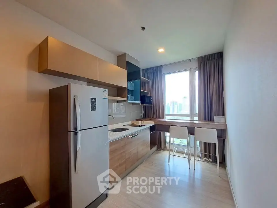 Modern kitchen with sleek cabinetry and city view, featuring a fridge and breakfast bar.