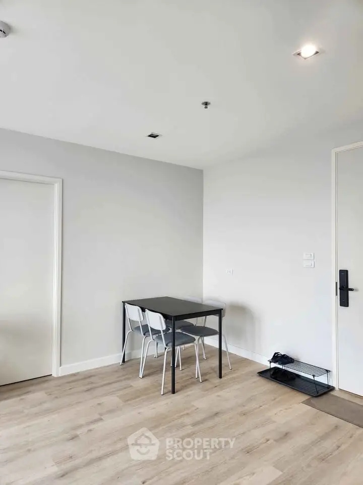 Modern minimalist dining area with sleek black table and white chairs on light wood flooring.