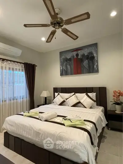 Elegant bedroom with modern decor, featuring a ceiling fan, stylish artwork, and cozy bedding.