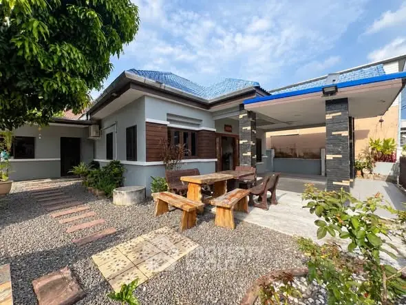 Charming single-story home with blue roof, spacious patio, and lush garden, perfect for outdoor living.