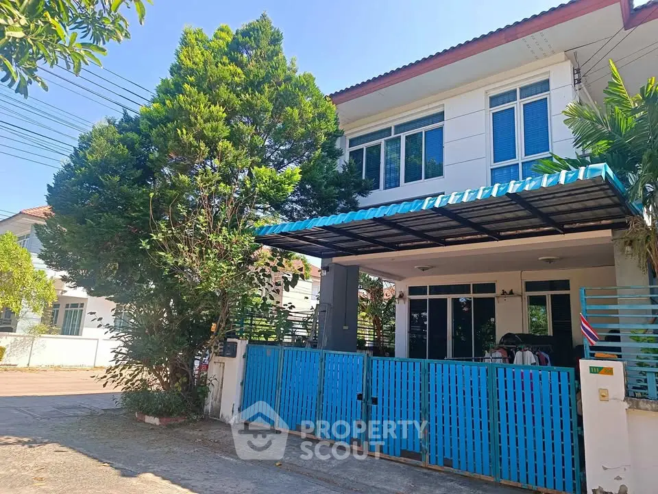 Charming two-story house with blue gate and lush greenery in a serene neighborhood.