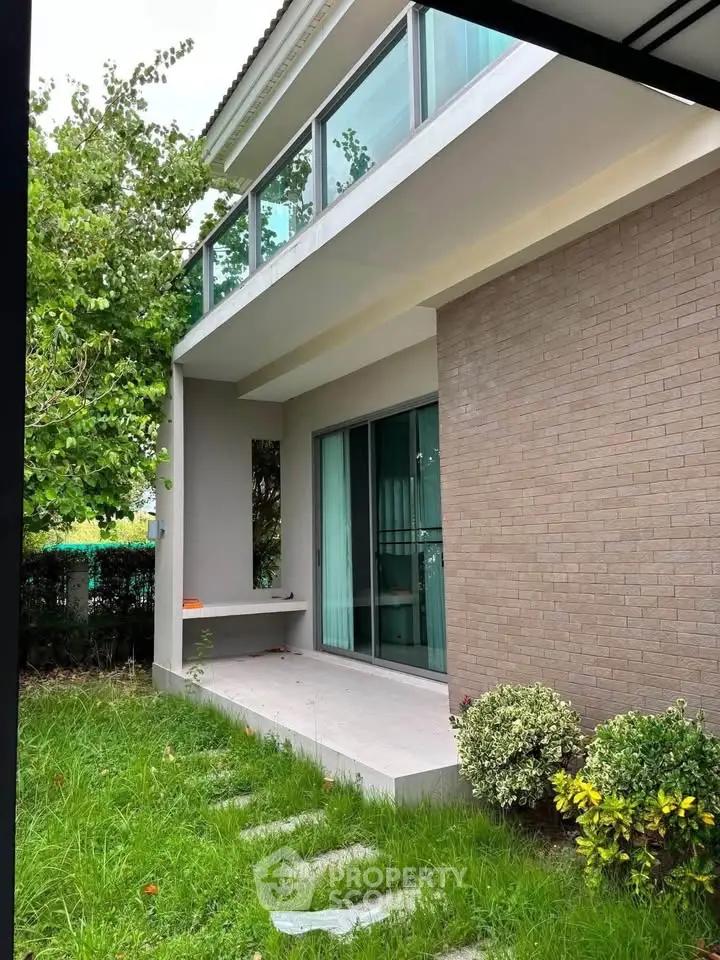 Modern two-story house with glass balcony and lush green garden