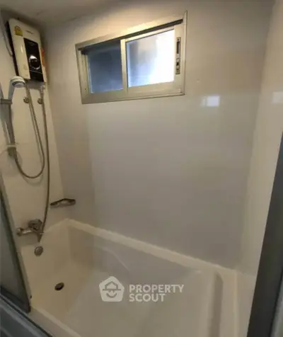 Modern bathroom with bathtub and shower, featuring a sleek design and natural light from a small window.
