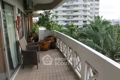 Spacious balcony with seating and lush greenery offering a serene view in a modern apartment.