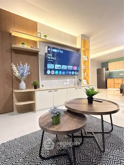 Modern living room with stylish decor and open kitchen layout, featuring a wall-mounted TV and elegant wooden furniture.