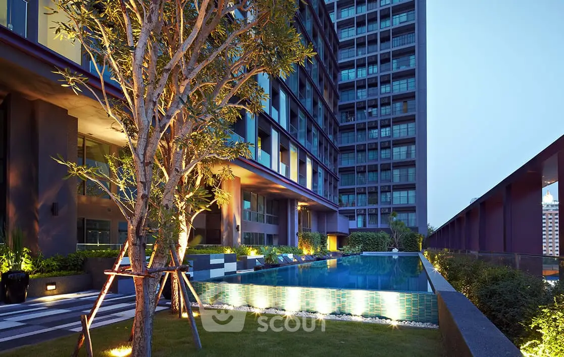 Luxurious modern apartment building with illuminated pool and lush garden.
