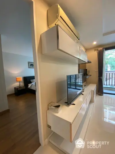 Sleek modern living space with glossy white entertainment unit, warm wooden floors, and a cozy seating area leading to a sunlit balcony.