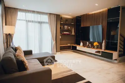 Modern living room with large sofa and entertainment center, featuring floor-to-ceiling windows.