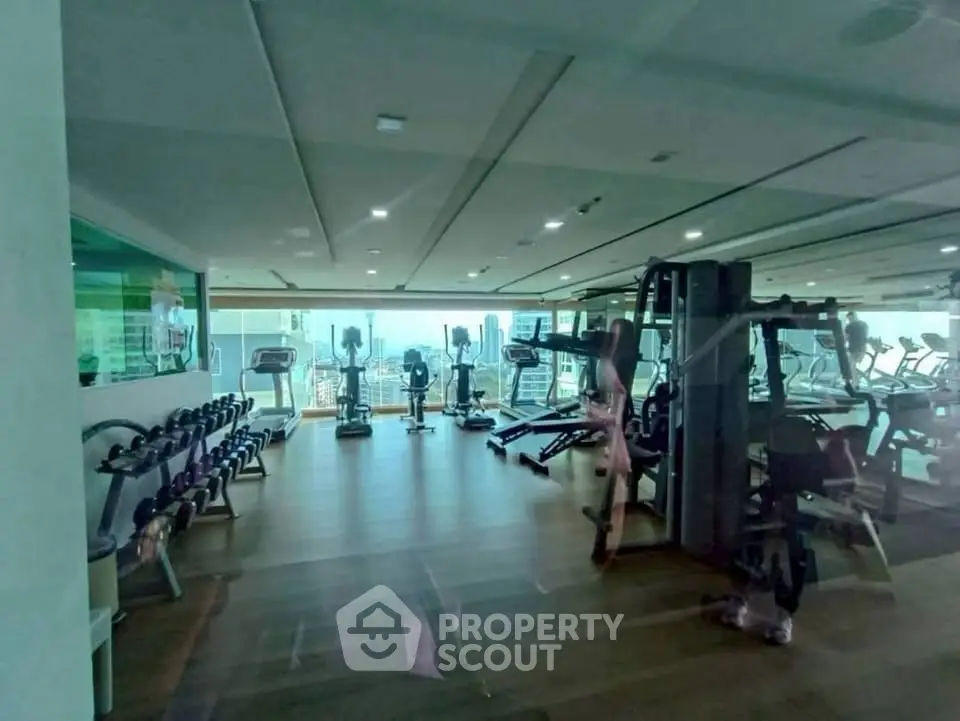 Spacious gym with modern equipment and city view in luxury apartment building.