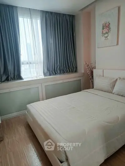 Cozy bedroom with elegant curtains and floral artwork, featuring a comfortable bed and wooden flooring.
