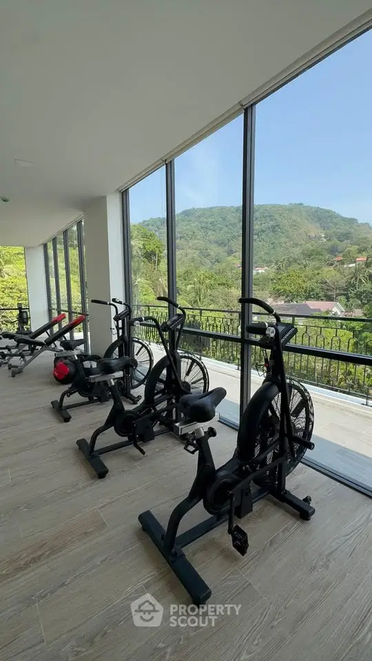 Modern gym with scenic mountain view through large windows, featuring exercise bikes and equipment.