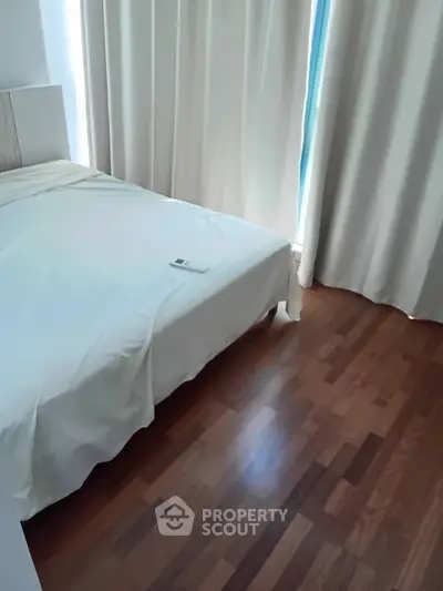 Cozy bedroom with wooden flooring and natural light through curtains.