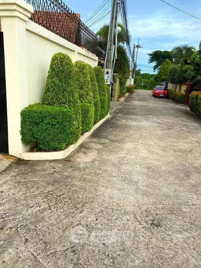 Charming residential street with manicured hedges and parked red car, ideal for tranquil living.