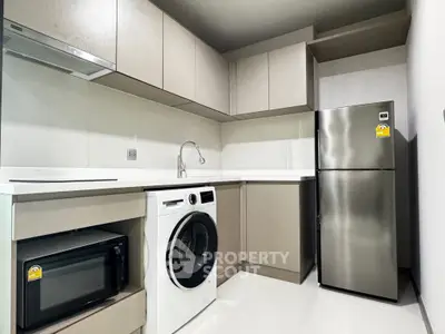 Modern kitchen with sleek appliances including fridge, washing machine, and microwave in a compact layout.