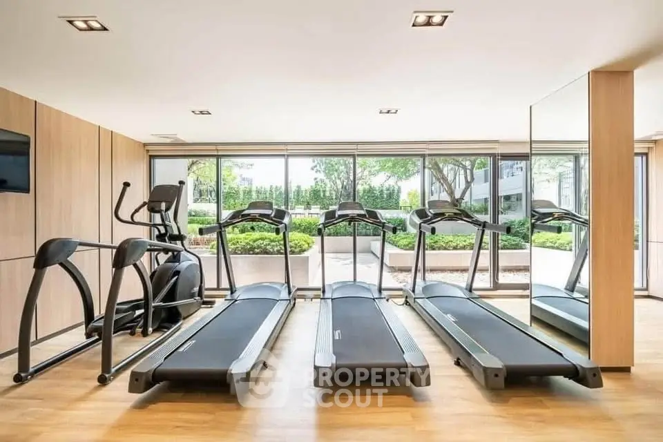 Modern gym with treadmills and exercise equipment in a bright, spacious room with garden view.
