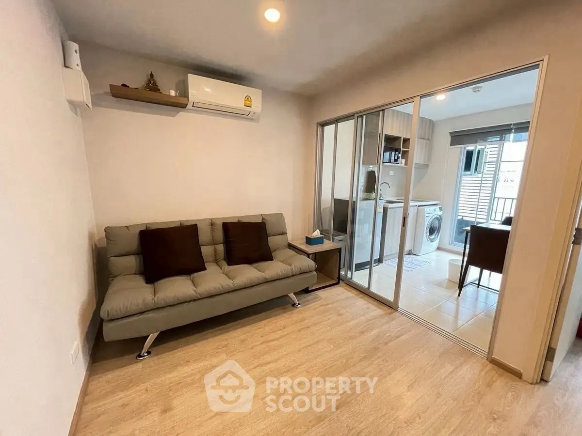 Modern living room with sofa and sliding glass doors leading to kitchen area.