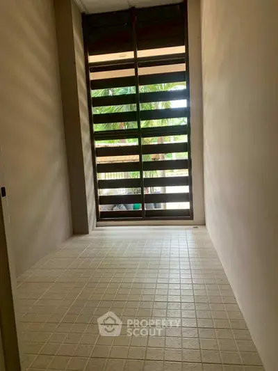 Spacious tiled balcony with wooden slatted windows offering a serene garden view.