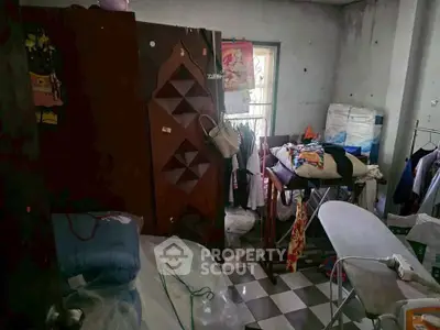 Cluttered storage room with ironing board and clothes racks in a residential property.
