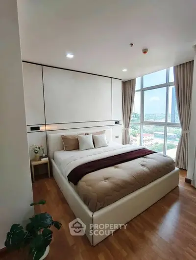 Luxurious bedroom with large windows offering stunning city views, featuring elegant decor and cozy bedding.