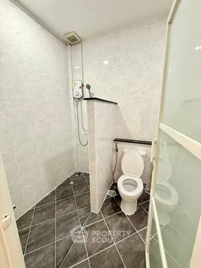Modern bathroom with shower and toilet, featuring tiled walls and floors.