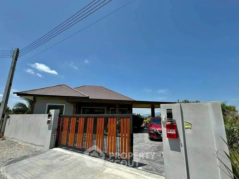 Modern single-story house with gated entrance and driveway under clear blue sky.