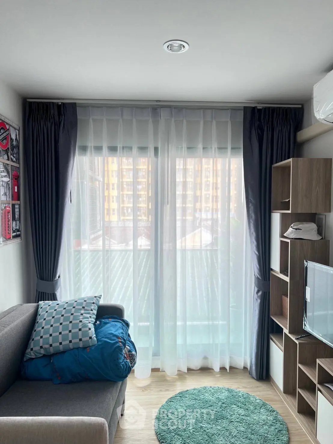 Cozy living room with large window, modern sofa, and stylish shelving unit in a bright apartment.