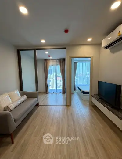 Modern living room with wooden flooring, cozy sofa, and large windows offering natural light.