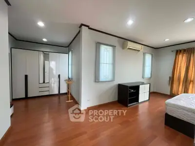 Spacious bedroom with wooden flooring and modern furniture in a well-lit apartment.