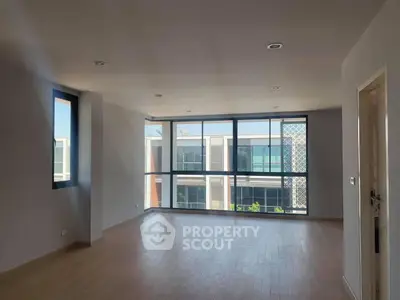 Spacious modern living room with large windows and wooden flooring, offering ample natural light.