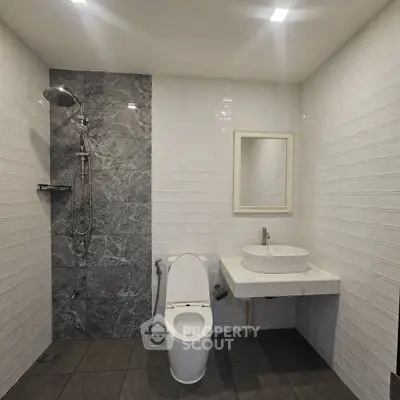 Modern bathroom with sleek design featuring a shower, toilet, and stylish sink.