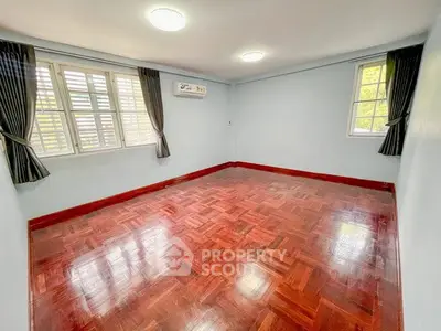 Spacious empty room with polished wooden floors and large windows, perfect for customization.