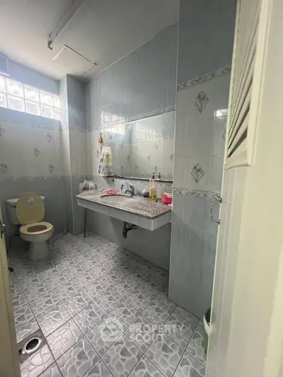 Spacious bathroom with tiled walls and floor, featuring a large mirror and modern fixtures.