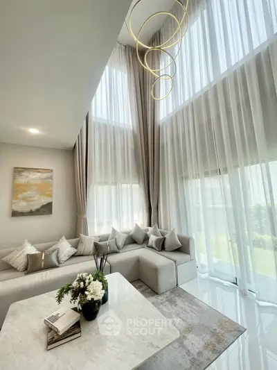 Luxurious living room with high ceilings, elegant chandelier, and large windows with sheer curtains.