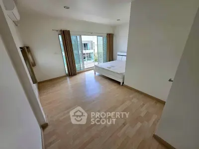 Spacious bedroom with wooden flooring and large windows offering natural light and a view.