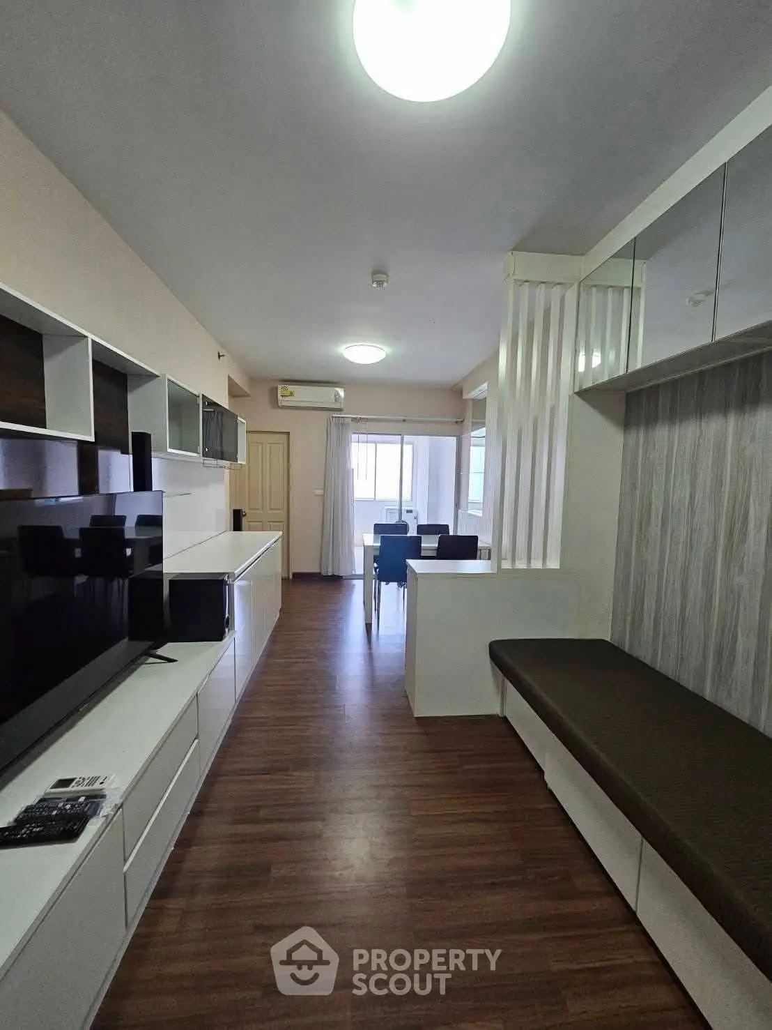 Modern living room with sleek furniture and dining area, featuring stylish wooden flooring and ample natural light.