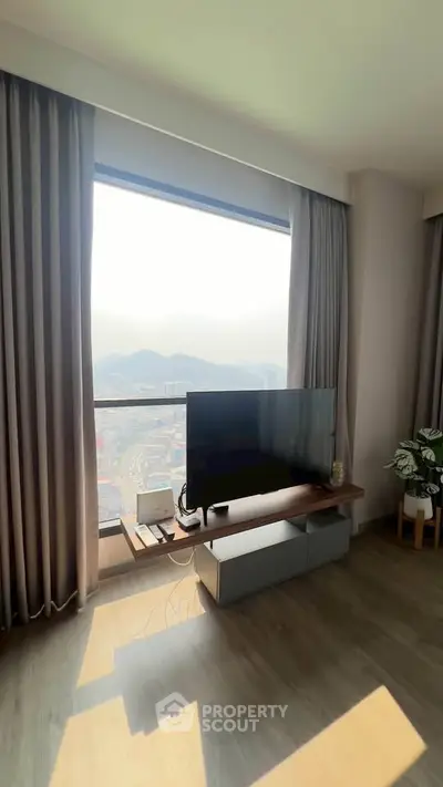 Modern living room with large window offering stunning city view, featuring sleek TV setup and elegant curtains.