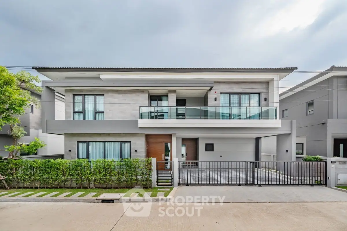 Modern two-story house with sleek design and spacious balcony, featuring a well-maintained front yard and driveway.