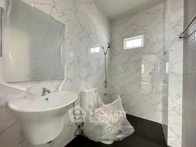 Modern bathroom with sleek white fixtures and marble-patterned walls, featuring a wall-mounted sink and shower area.