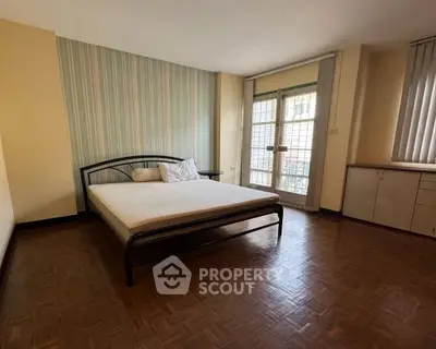 Spacious bedroom with large window and parquet flooring in modern apartment.