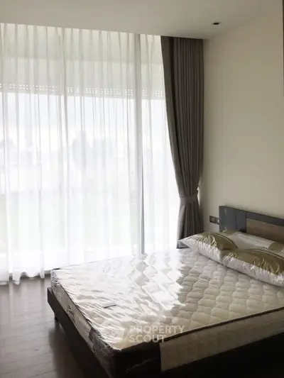 Spacious bedroom with large windows and city view, featuring a comfortable bed and elegant curtains.