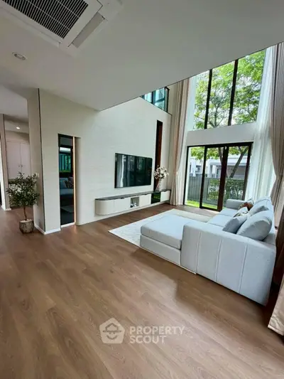 Spacious modern living room with high ceilings and large windows overlooking a garden.