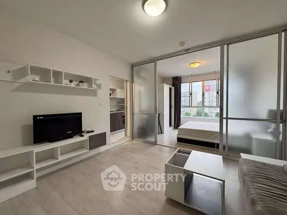 Modern open-plan living room with sliding glass doors leading to a cozy bedroom, featuring sleek furniture and ample natural light.