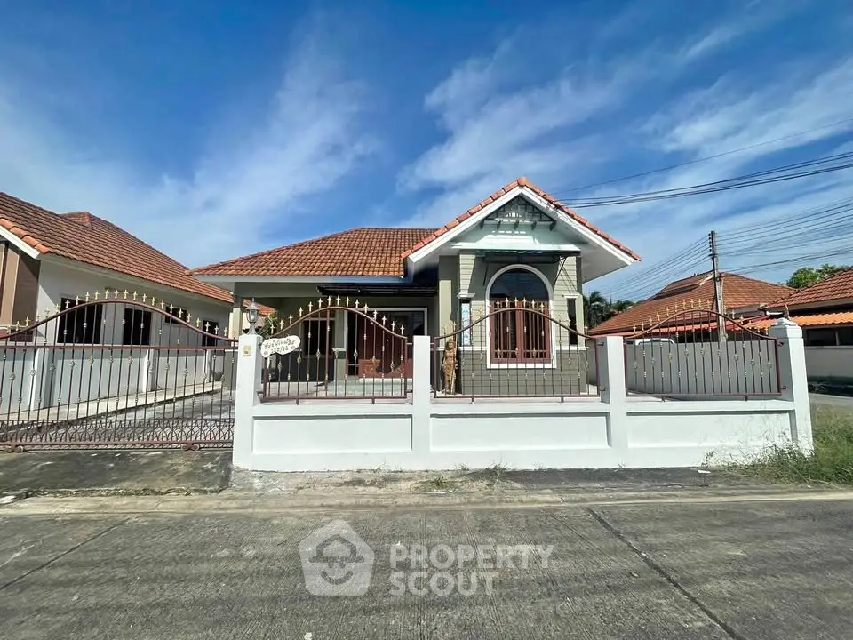 Charming single-story house with red-tiled roof and gated entrance under clear blue sky.